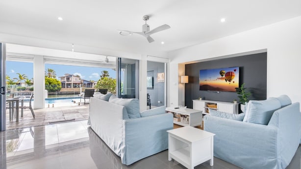 A modern living room with a pool view, a ceiling fan, and a flat-screen TV. - Tranquillit, TOP NOTCH (BANKSIA BEACH)