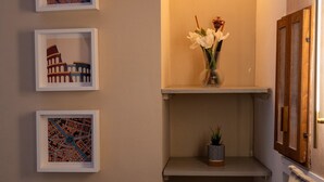 A hallway with framed cityscape artwork, a shelf with a vase of flowers, and a small potted plant. - Small oasis in the heart of Rome (Roma)