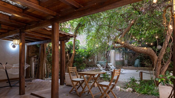 An outdoor wooden deck with a table and chairs, surrounded by greenery and trees. - Small oasis in the heart of Rome (Roma)