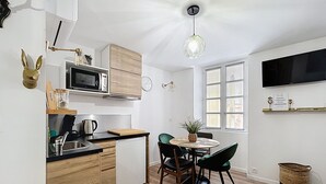 Moderni keittiö, jossa on puiset kaapit, mikroaaltouuni sekä ruokailutila, jossa on pöytä ja tuolit.