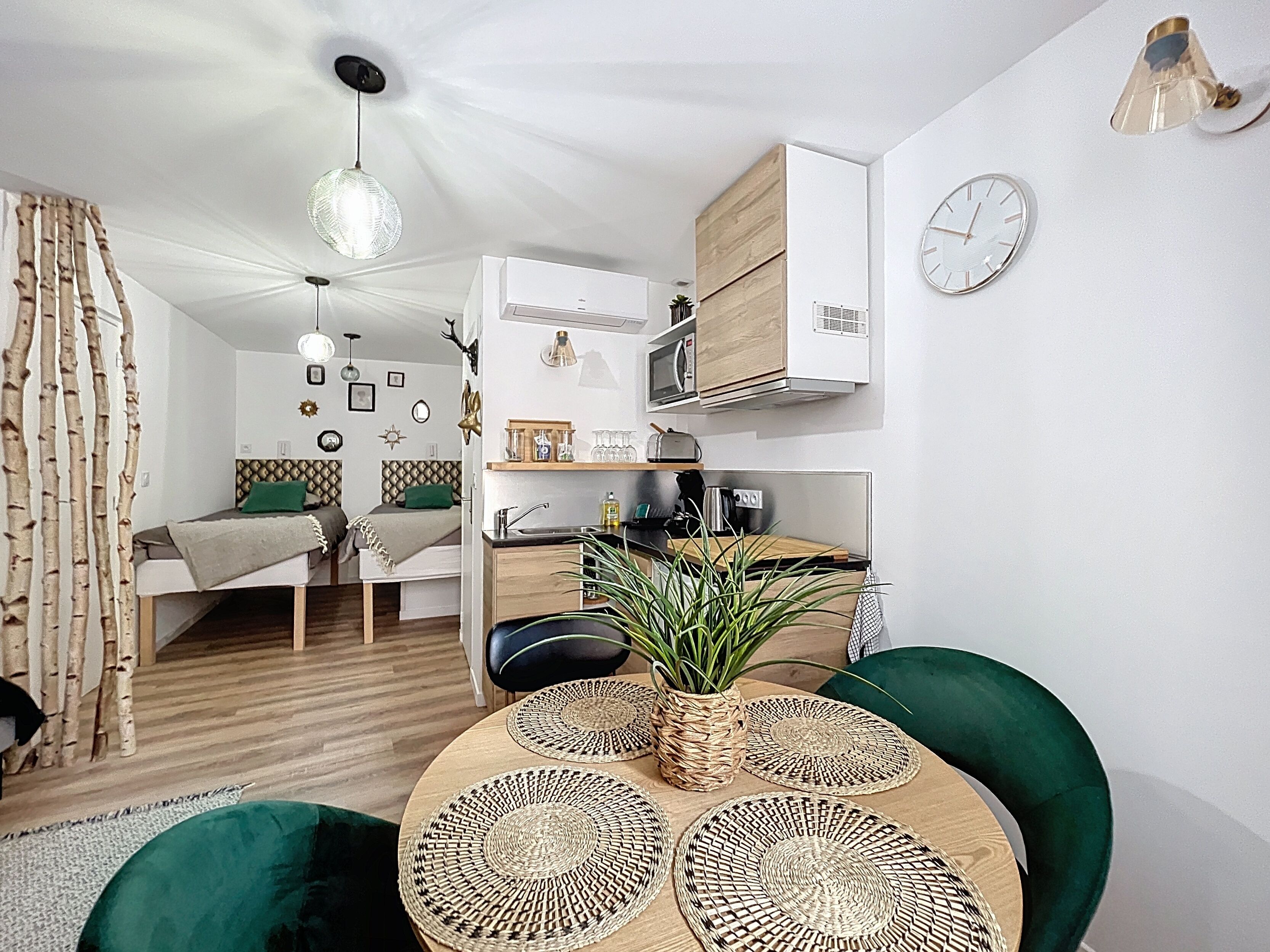 Un espacio habitable moderno y funcional, con kitchenette, comedor con mesa redonda y cama con almohada verde.
