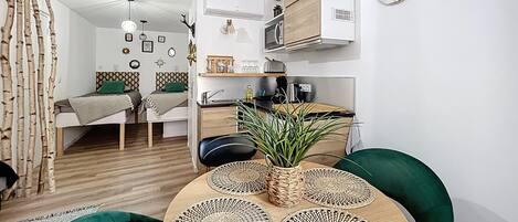 Un espacio habitable moderno y funcional, con kitchenette, comedor con mesa redonda y cama con almohada verde.