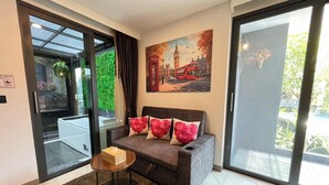 A modern living room with a grey sofa, a small wooden table, and a painting of a red double-decker bus. - A201 - 1 Bedroom 1 Bathroom with private bubble Jacuzzi, garden at Ao Nang Beach (Tambon Ao Nang)