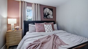 A bedroom with a bed, bedside table, lamp, and a window with curtains.