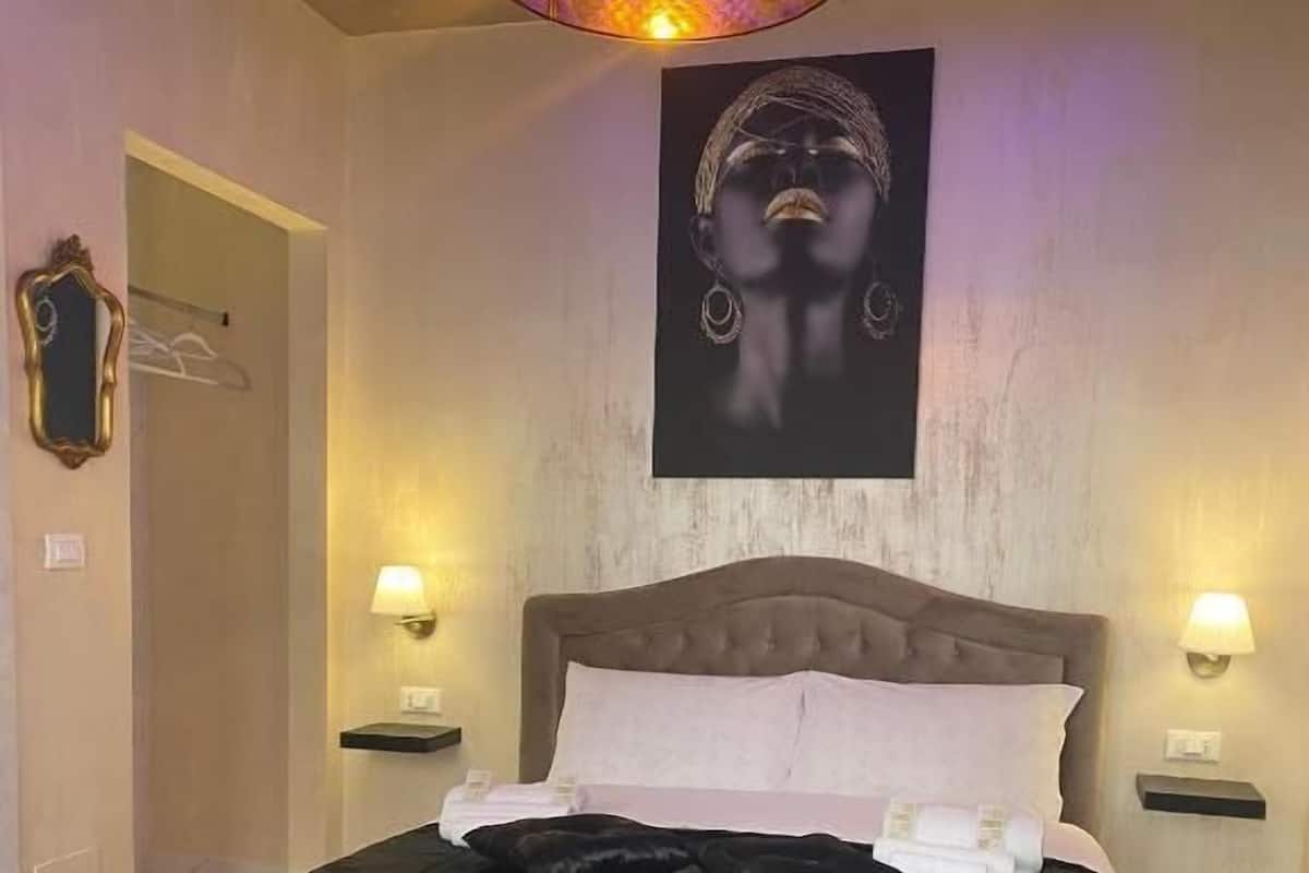 A bedroom with a large bed, two bedside lamps, a ceiling light, and a wall-mounted artwork.