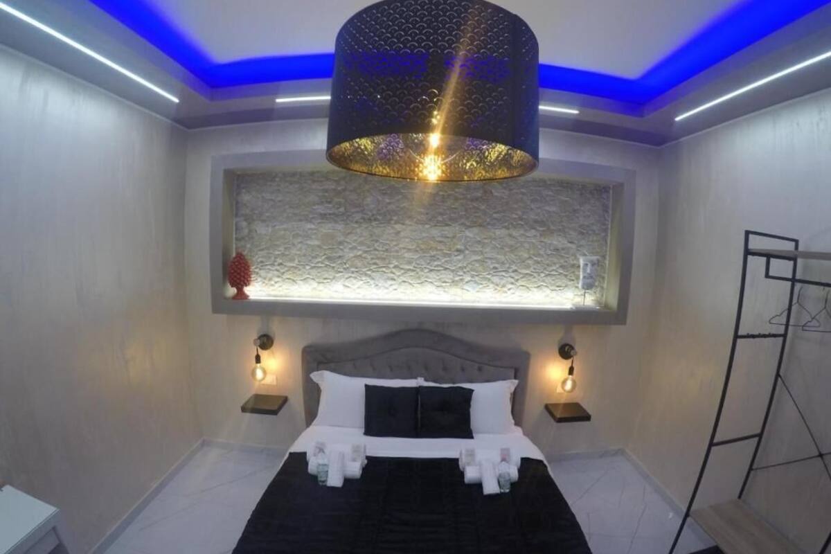 A modern bedroom with a bed, bedside lamps, a textured wall, and a hanging light fixture.