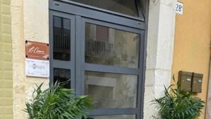 Entrada de un edificio con puerta de cristal, dos plantas en macetas y un cartel en la pared.