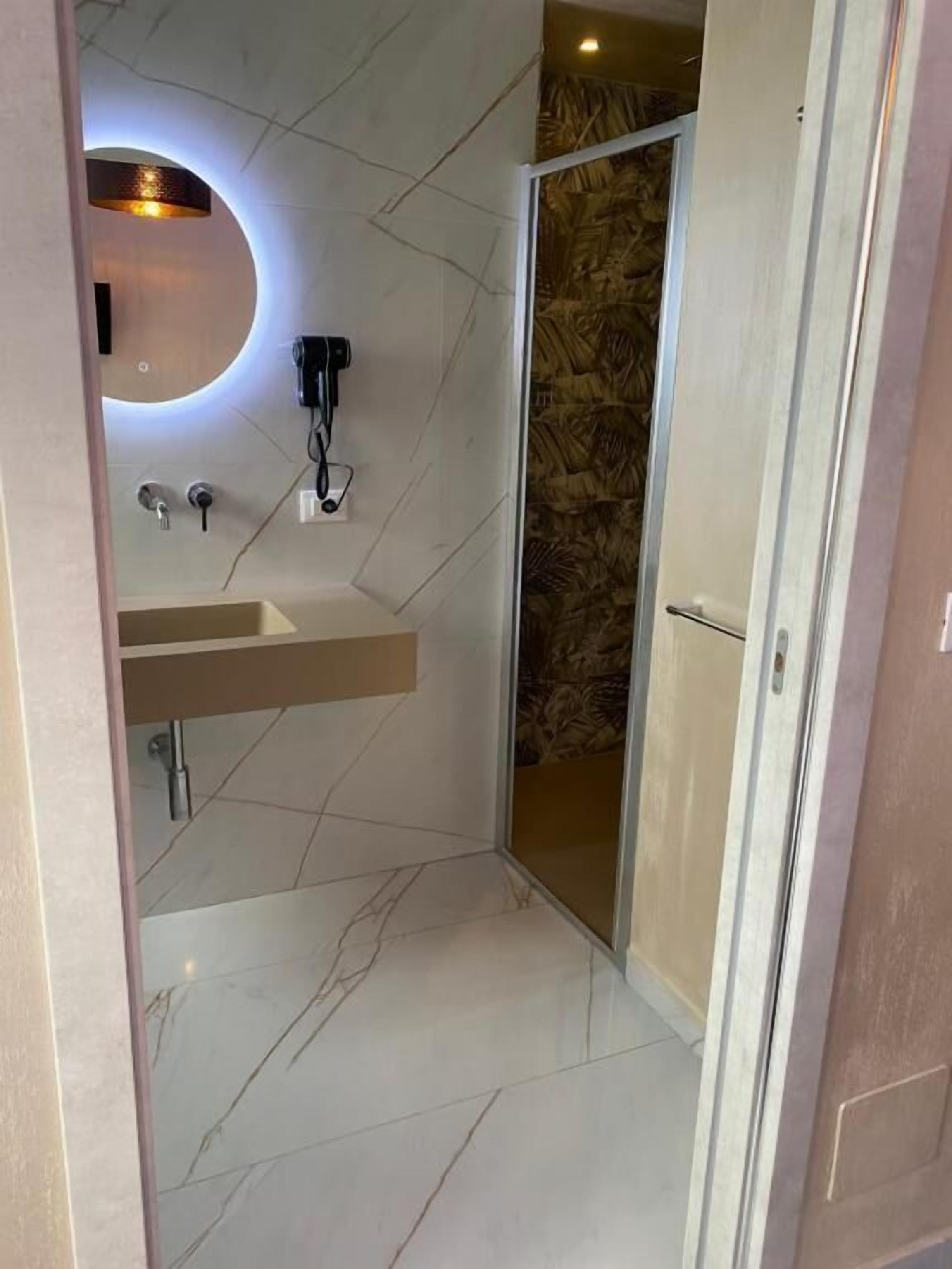 Ein modernes Badezimmer mit Marmorboden, Waschbecken mit Spiegel und Duschbereich.