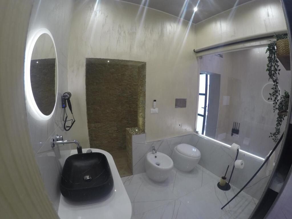 Un bany modern amb un mirall gran, un lavabo negre, dues vàteres i una zona de banyera.