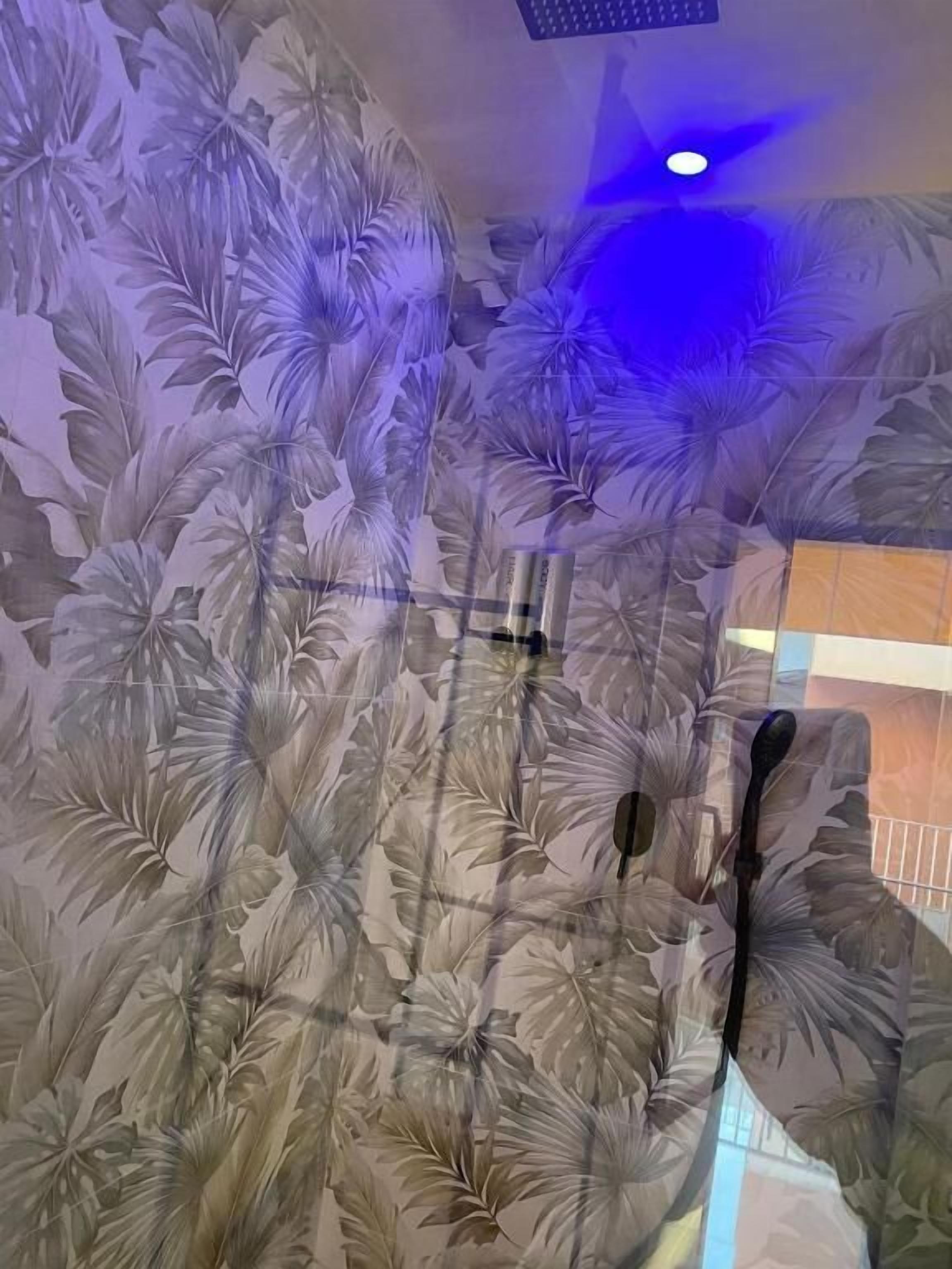 Una habitación con papel tapiz estampado con motivos tropicales, un ventilador de techo y una lámpara visible.