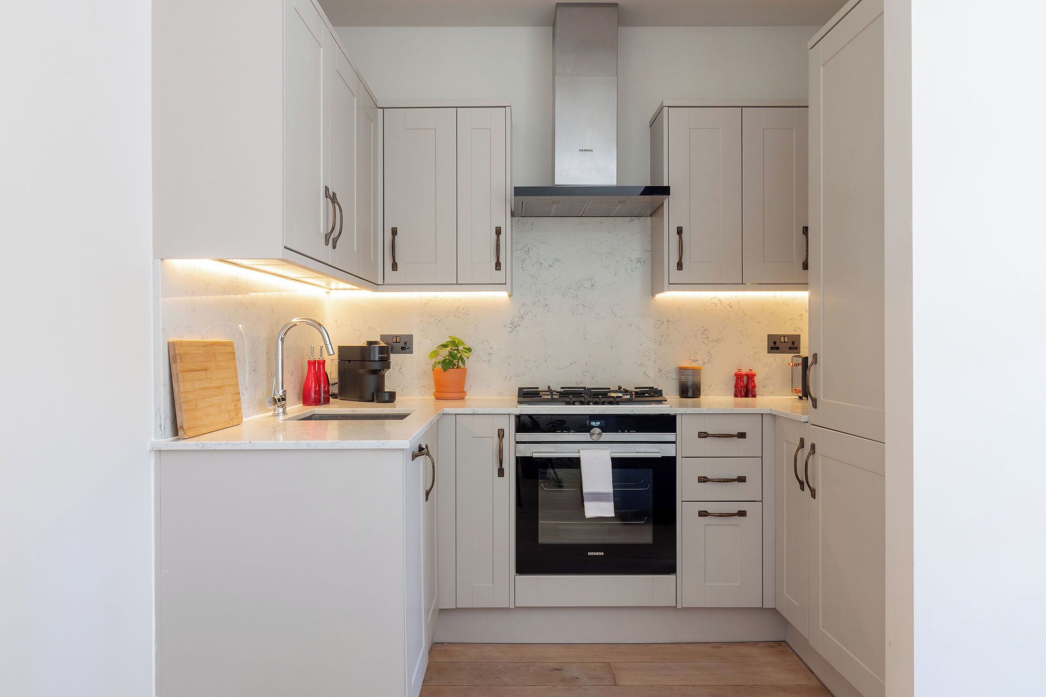 A modern kitchen with white cabinets, a stainless steel range hood, and a built-in oven.