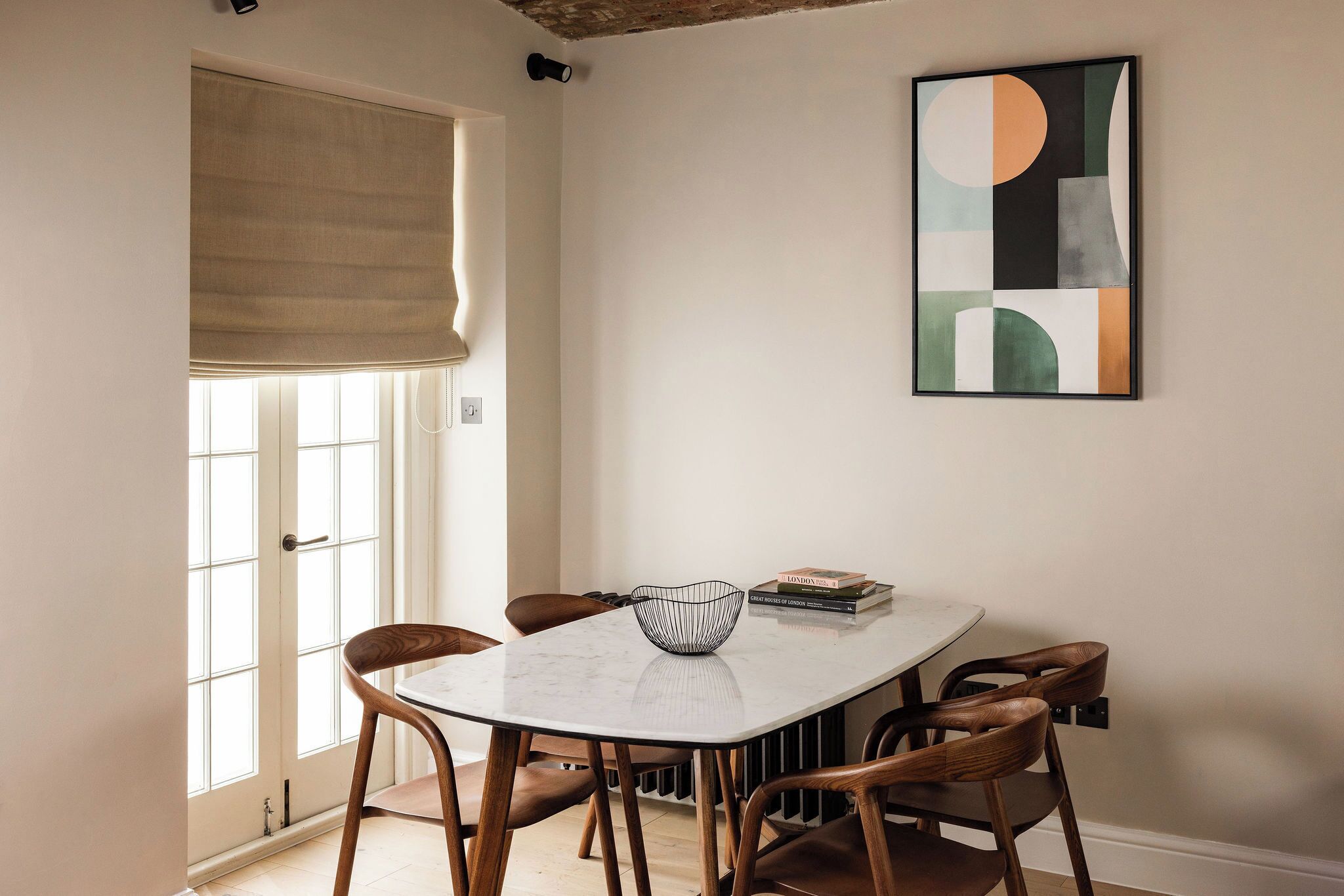 Zona pranzo con tavolo in marmo bianco, sedie di legno, una ciotola e un quadro astratto incorniciato appeso al muro.