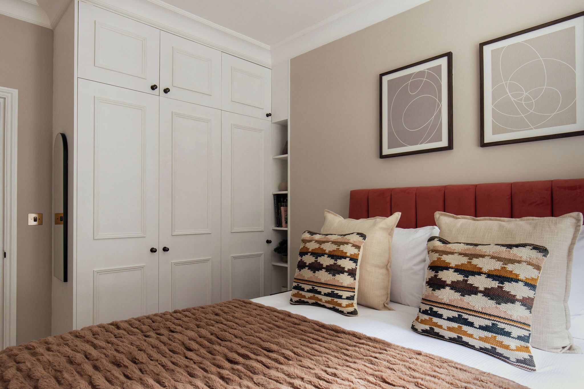 Une chambre à coucher avec un grand lit, une tête de lit rouge et deux tableaux abstraits encadrés accrochés au mur.