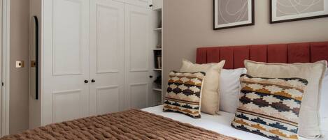 Une chambre à coucher avec un grand lit, une tête de lit rouge et deux tableaux abstraits encadrés accrochés au mur.