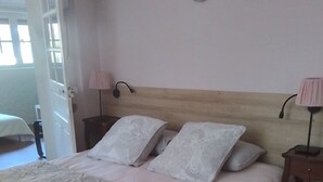 Un letto con una testiera in legno, due comodini con lampade e una porta che dà su un'altra stanza.