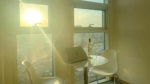 Ein Zimmer mit einem Laptop auf einem kleinen Tisch, zwei weißen Stühlen, einer Flasche und einem Glas.