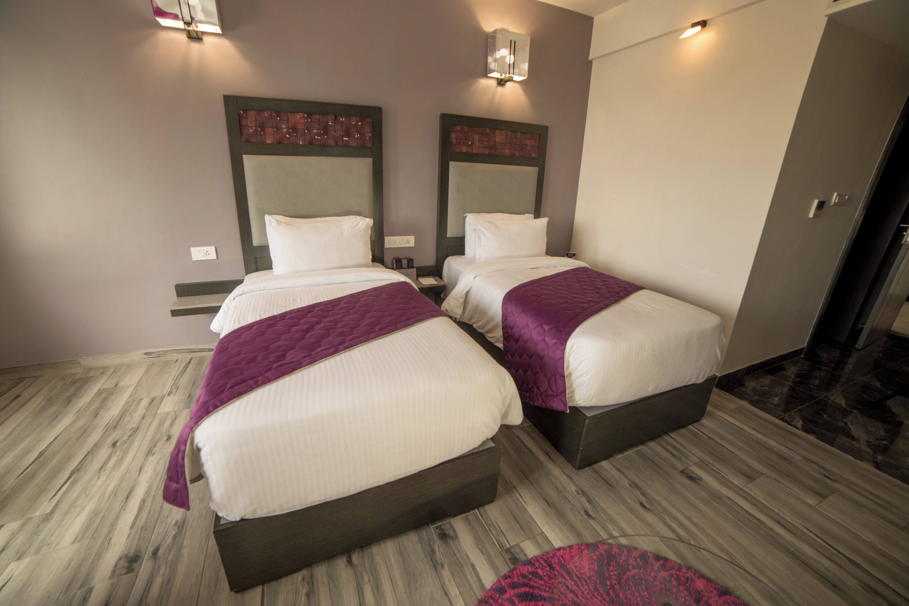 A hotel room with two beds, wooden flooring, and a small rug.