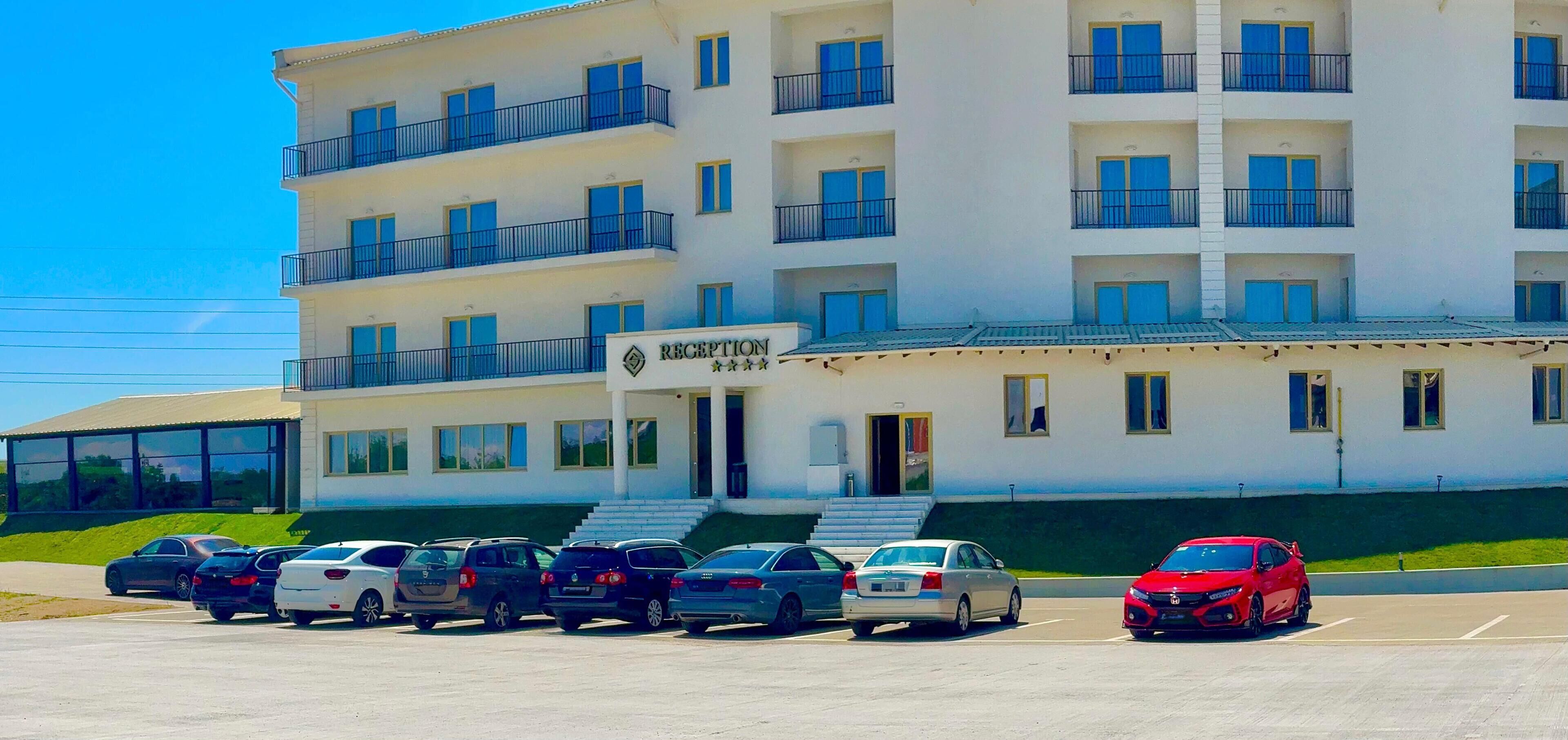 A multi-story hotel with a reception area, parking lot, and a red car parked in front.