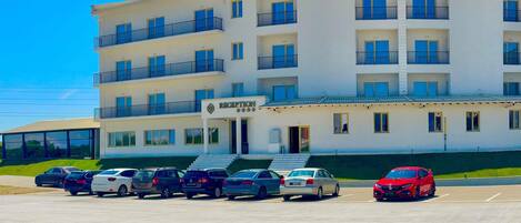 A multi-story hotel with a reception area, parking lot, and a red car parked in front.