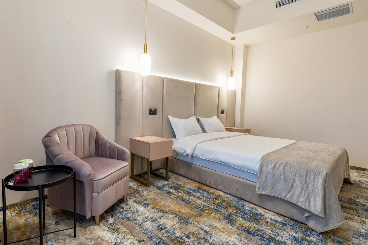 Una habitación de hotel con una cama, una silla, una mesita de noche y una lámpara.