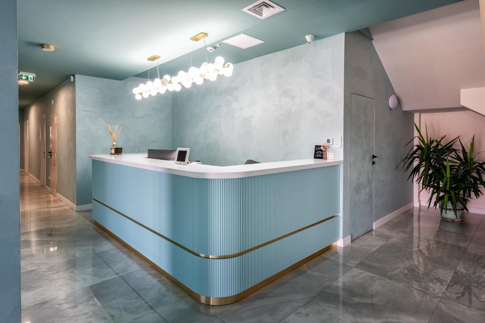 A reception area with a light blue counter, a modern chandelier, and a potted plant.