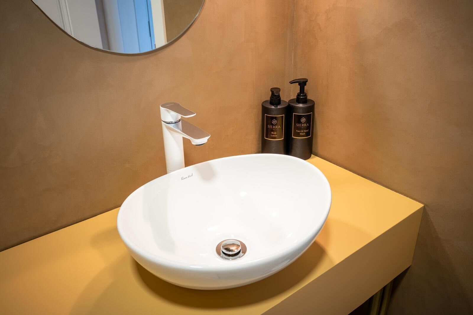 A bathroom with a white sink, a modern faucet, and two bottles of Sierra body lotion and hand wash.