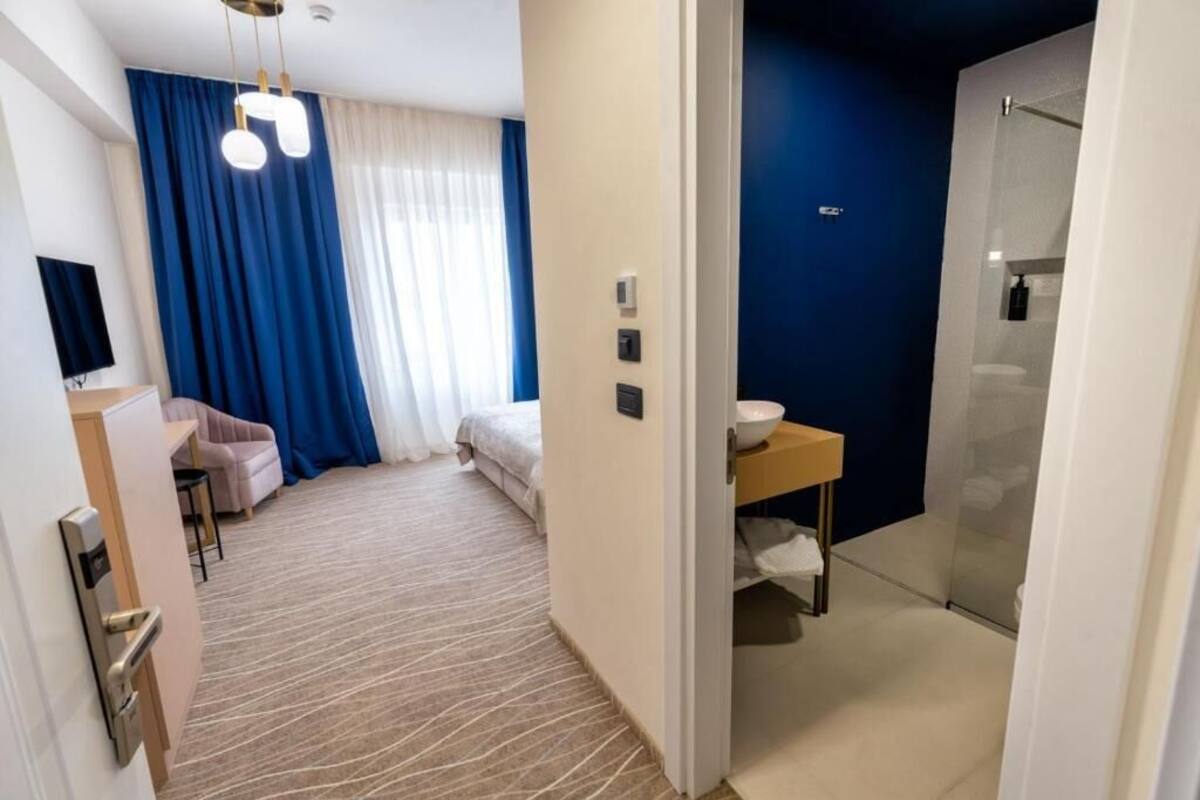 Habitación de hotel con cama, escritorio, silla, mesita con un tazón, espejo y zona de ducha.