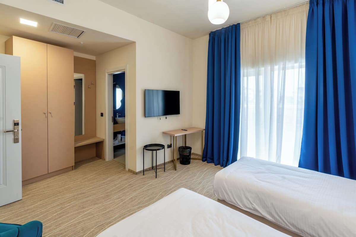 Habitación de hotel con dos camas, televisión, escritorio y armario.