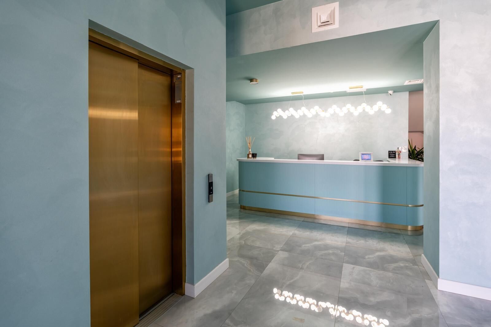 A reception area with a blue counter, a reception desk, and a wall-mounted light fixture.