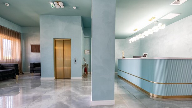 A modern lobby with a reception desk, a gold elevator, and a marble floor. - Hotel Sierra (Pitesti)