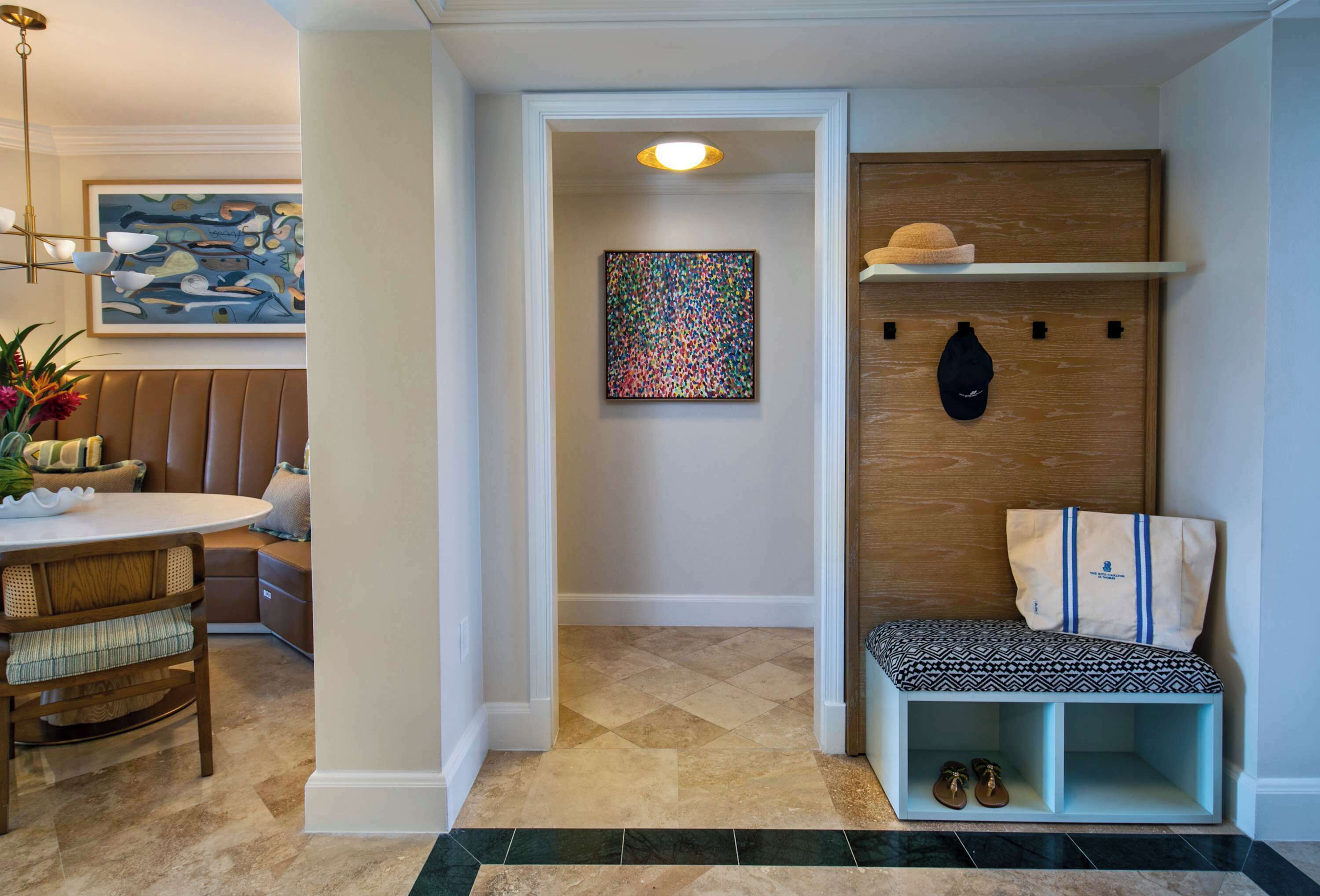 A cozy entryway with a bench, a wall-mounted shelf with a hat and a bag, and a colorful abstract painting.