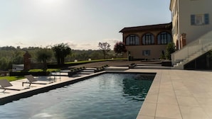 A swimming pool with lounge chairs, a building with arched windows, and a clear sky. - Vinea Relais (Dogliani)