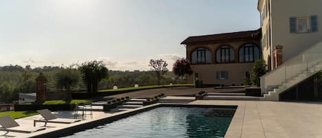 A swimming pool with lounge chairs, a building with arched windows, and a clear sky.