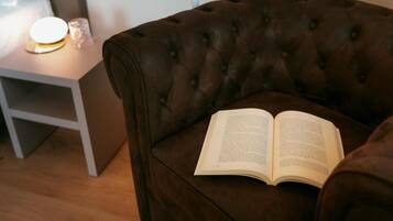 Un fauteuil marron à motifs capitonnés, avec un livre ouvert posé dessus, une table de chevet avec une lampe et un plancher en bois.