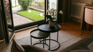 A cozy living room with a large window, a small round table with a potted plant, a sofa, and a chair. - Vinea Relais (Dogliani)