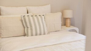 A bed with white bedding and striped pillows, a bedside lamp, and a white nightstand. - Mildura City Centre Escape 2 (Mildura)