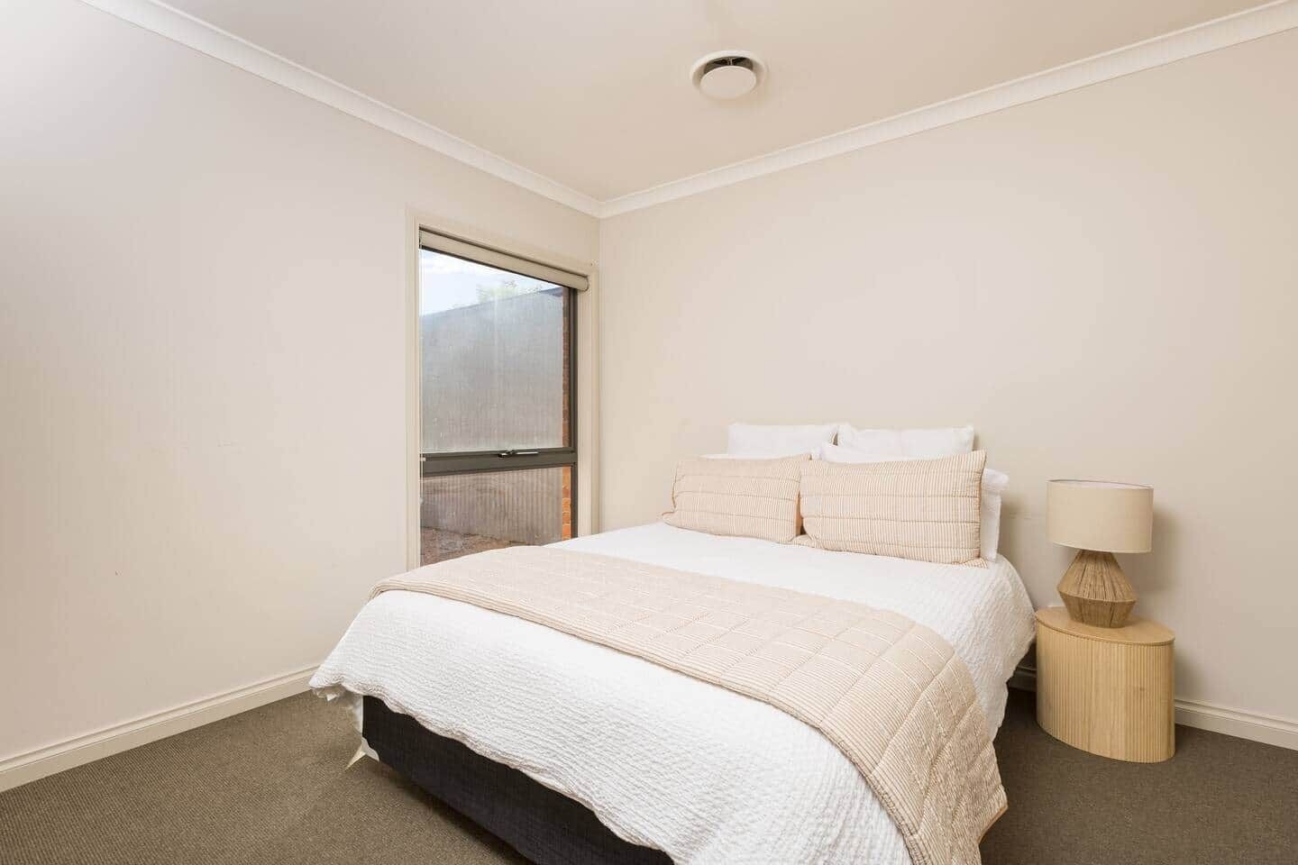 A bedroom with a bed, a nightstand, a lamp, and a window.