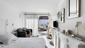 A hotel room with a bed, a desk, a chair, a TV, and a view of the outside.