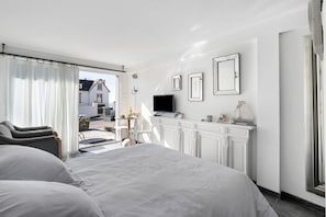 A hotel room with a large bed, a television, a small table with a lamp, and a view of the outside.