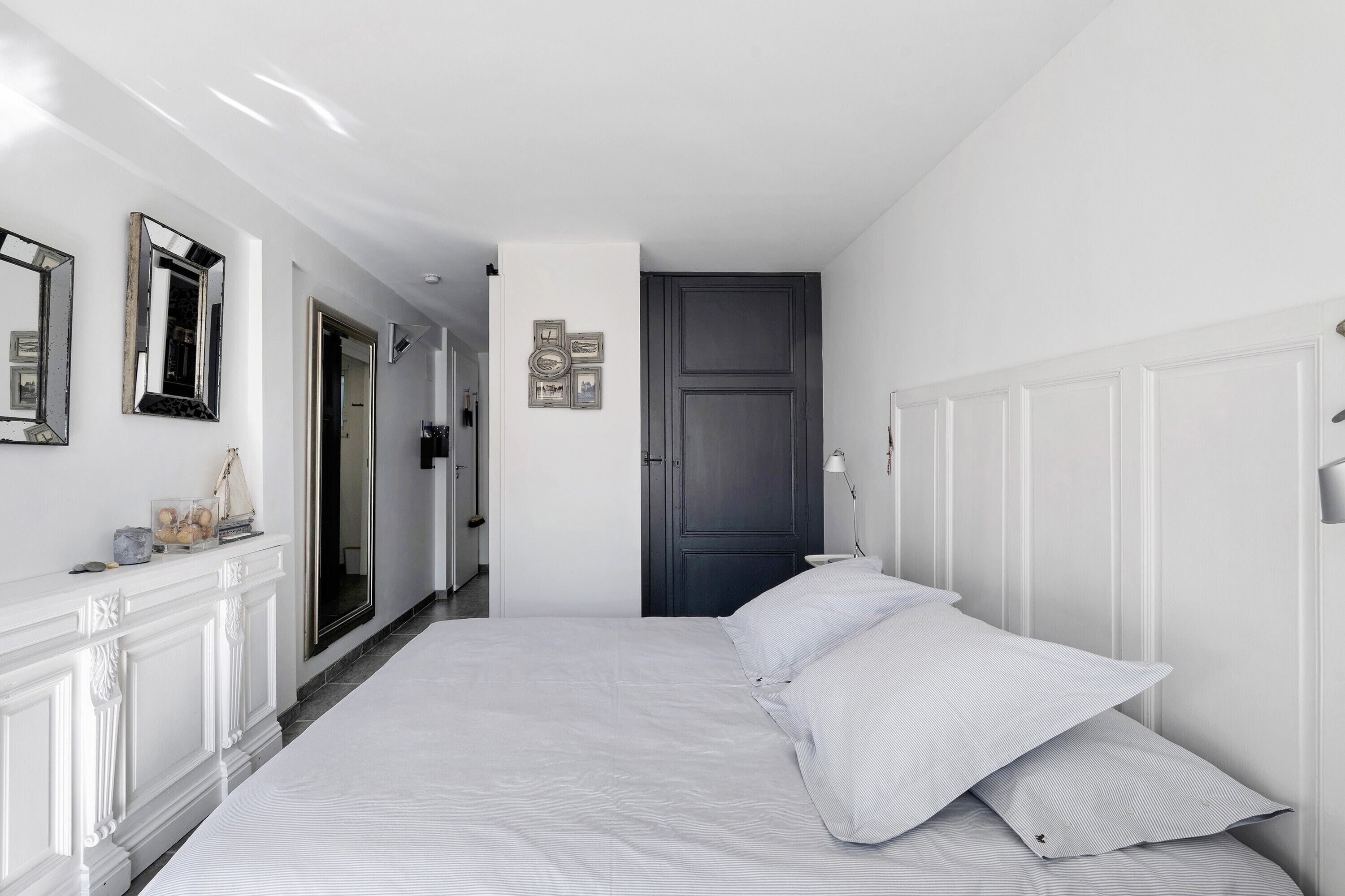 A bedroom with a bed, white walls, a dark door, and a hallway.