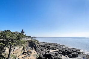 A coastal landscape with rocky terrain, a clear sky, and a distant building with a pointed roof.