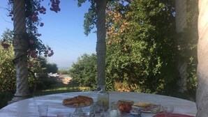 Ein runder Tisch draußen mit verschiedenen Speisen und Getränken, umgeben von Bäumen und blauem Himmel.