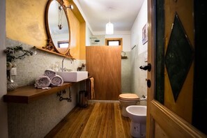 Une salle de bain avec un meuble-lavabo en bois, un grand miroir, un lavabo, des toilettes et un espace douche.