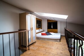 Une chambre avec un puits de lumière, un plancher en bois, un lit avec des oreillers, une armoire et une fenêtre.