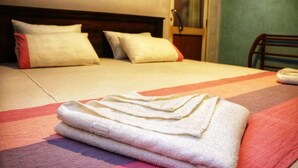 Een net opgemaakt bed met opgevouwen handdoeken, een houten hoofdbord en uitzicht op een kamer met een deur en een stoel.