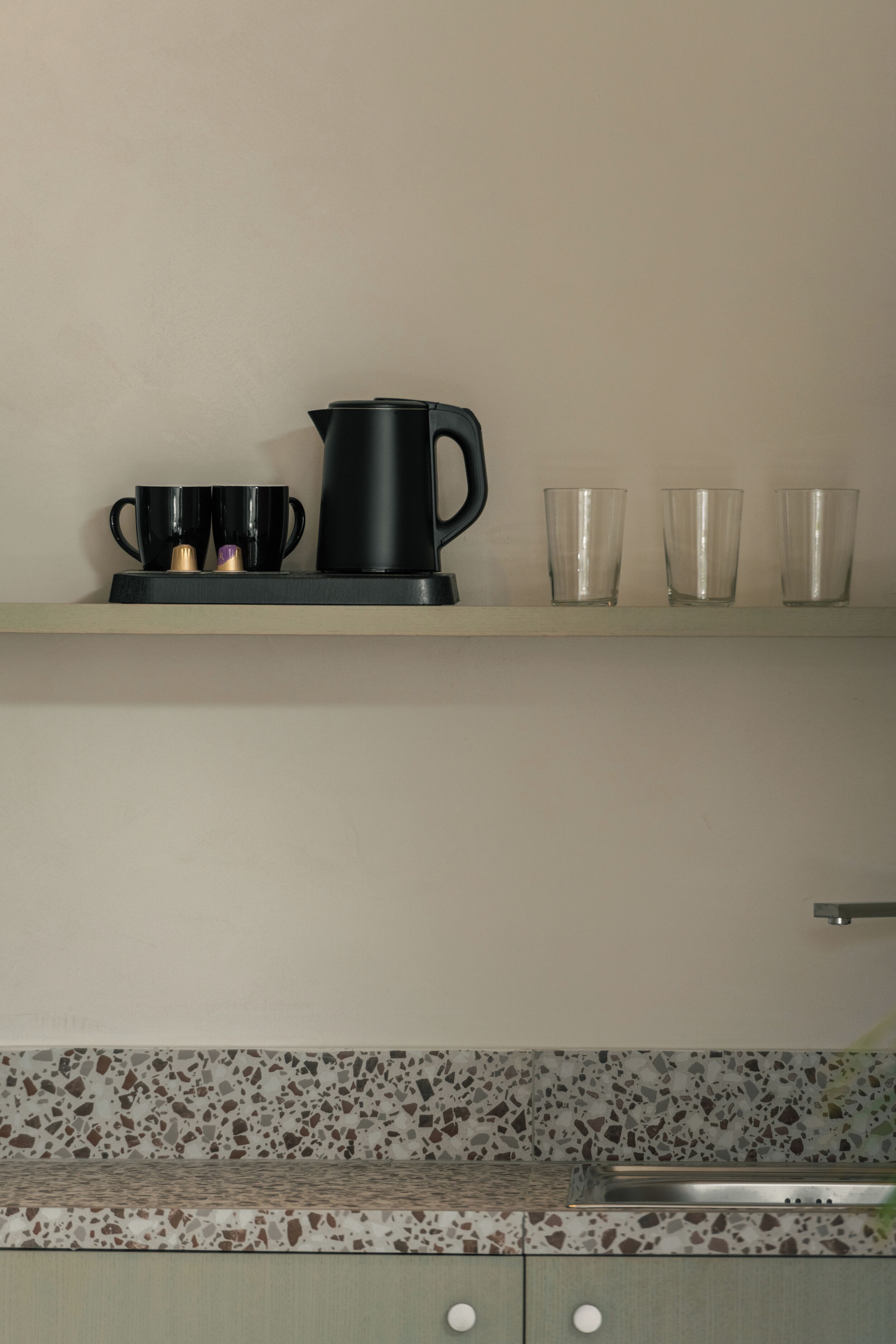 Una cocina con mostrador, una cafetera y tres tazas.