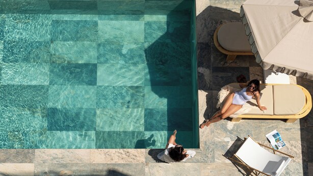 A rooftop pool with clear water, a lounge chair, and a sun umbrella. - FOS Luxury Suites (Nikiti)