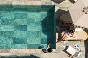 Una piscina en la azotea con agua cristalina, una tumbona y una sombrilla.