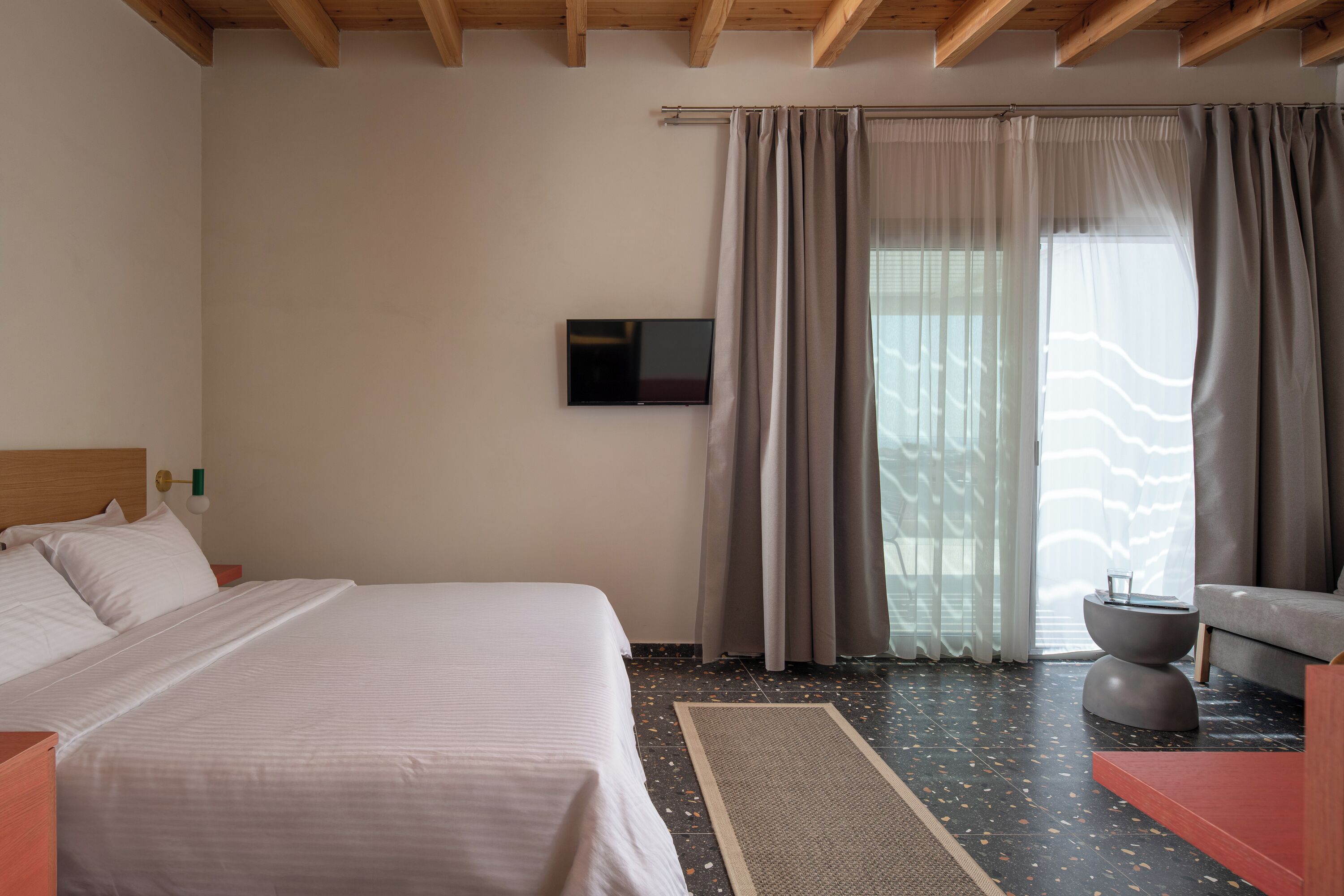 A modern hotel room with a large bed, a flat-screen TV, a sofa, and a dining table.