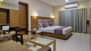 A hotel room with a bed, a desk, a chair, and a glass-top table. - Hotel Blue Orchid (Udaipur)